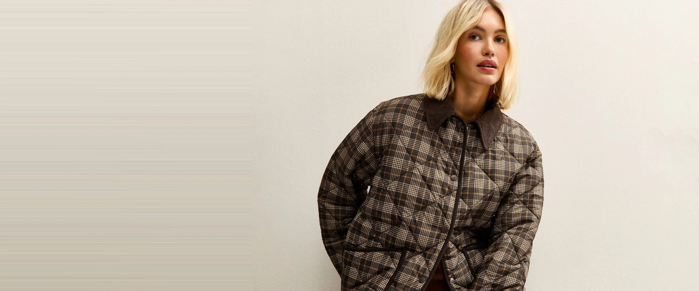 A model wearing an oversized brown checked quilted barn jacket with a corduroy collar, worn open over wide-leg blue jeans