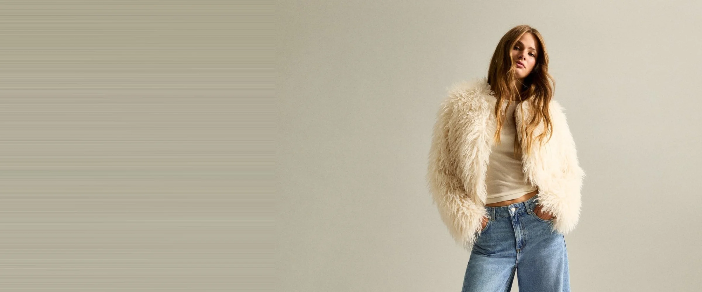 A model in light-wash barrel leg jeans with a cream faux fur jacket worn over a white vest top