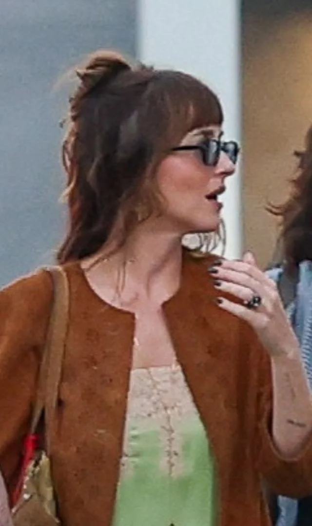 Dakota Johnson in a tan suede jacket worn open over an apple-green satin slip dress with cream lace trim, carrying a brown suede shoulder bag