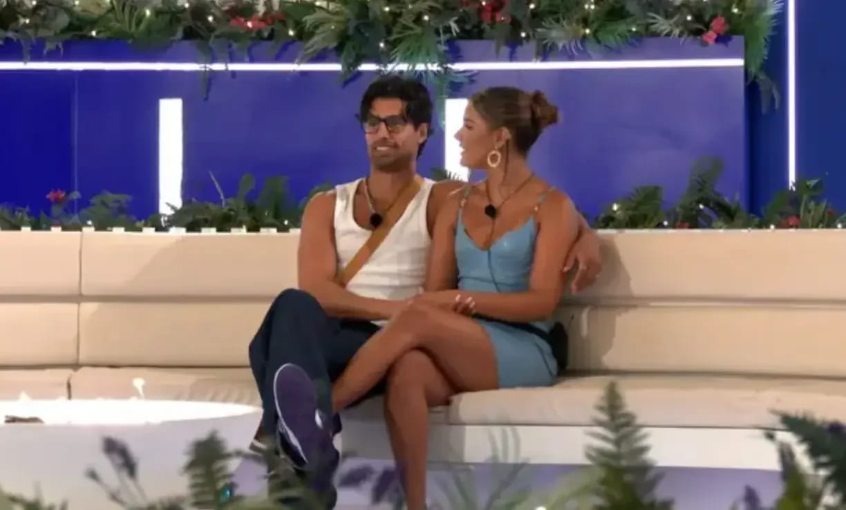 Mica Harris in a turquoise latex mini dress with gold buckle straps, sitting with Samraj at the villa firepit