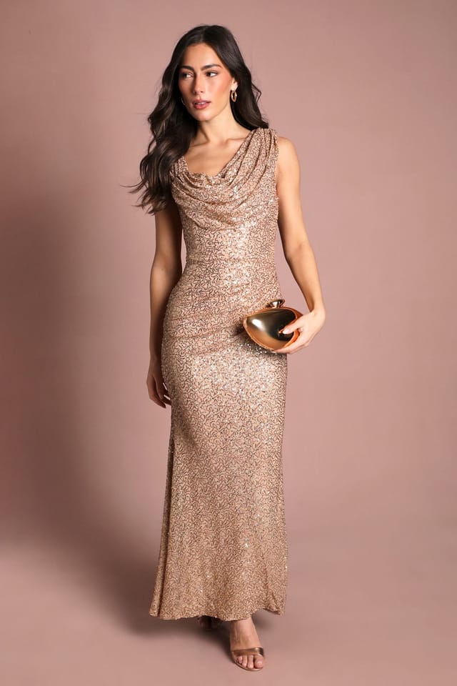 Model wearing a Coast gold sequin cowl-neck maxi dress, holding a gold clutch, against a dusky pink studio backdrop