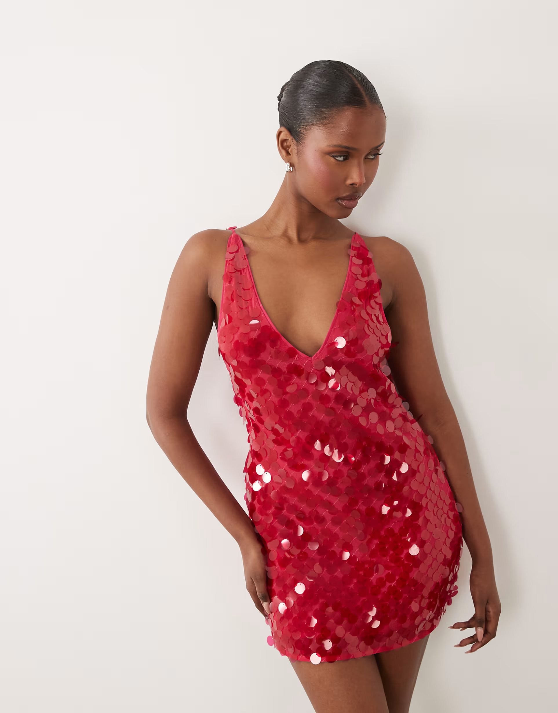 Model wearing an ASOS DESIGN cherry-red disc-sequin plunge mini dress against a pale grey studio backdrop